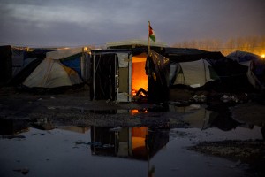 Un réfugié se repose autour d’un feu dans sa cabane de la zone nord de la Jungle de Calais.