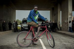 Manifestation en faveur des réfugiés. 1er octobre 2016 – Calais. Un jeune réfugié à vélo vient observer ce qu’il se passe.